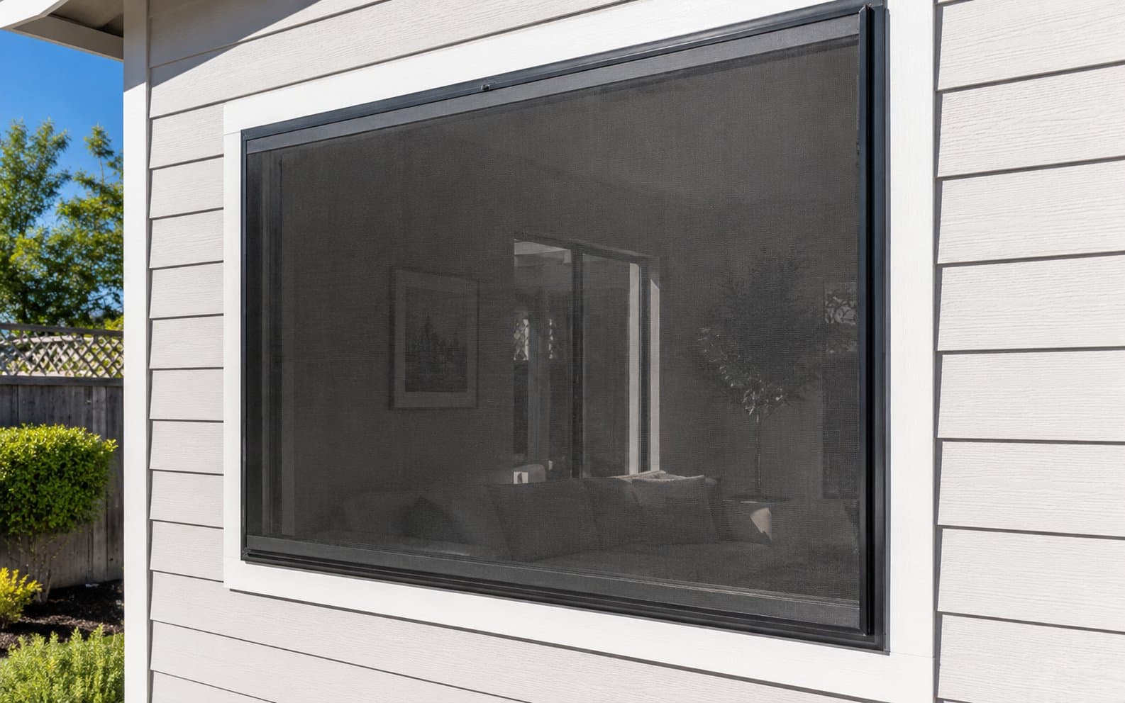 Exterior solar screen installed on a west-facing window, black aluminum frame, interior visible through the mesh